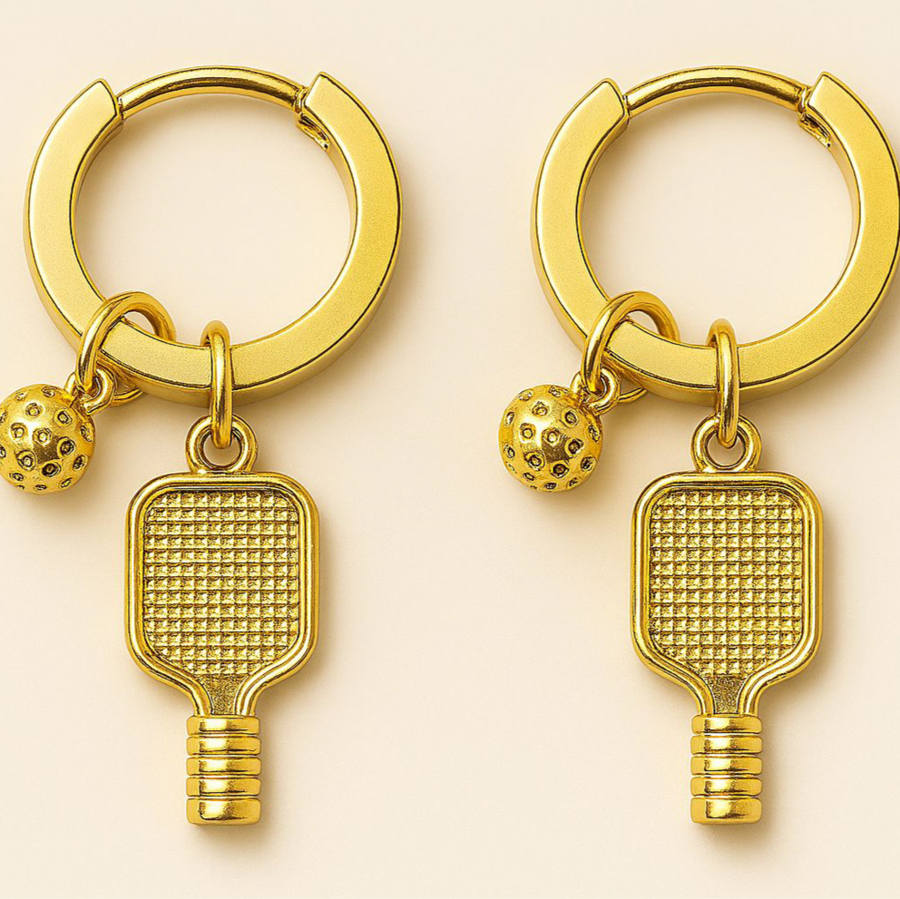 Gold hoop earrings with pickleball paddle and ball charms on a beige background