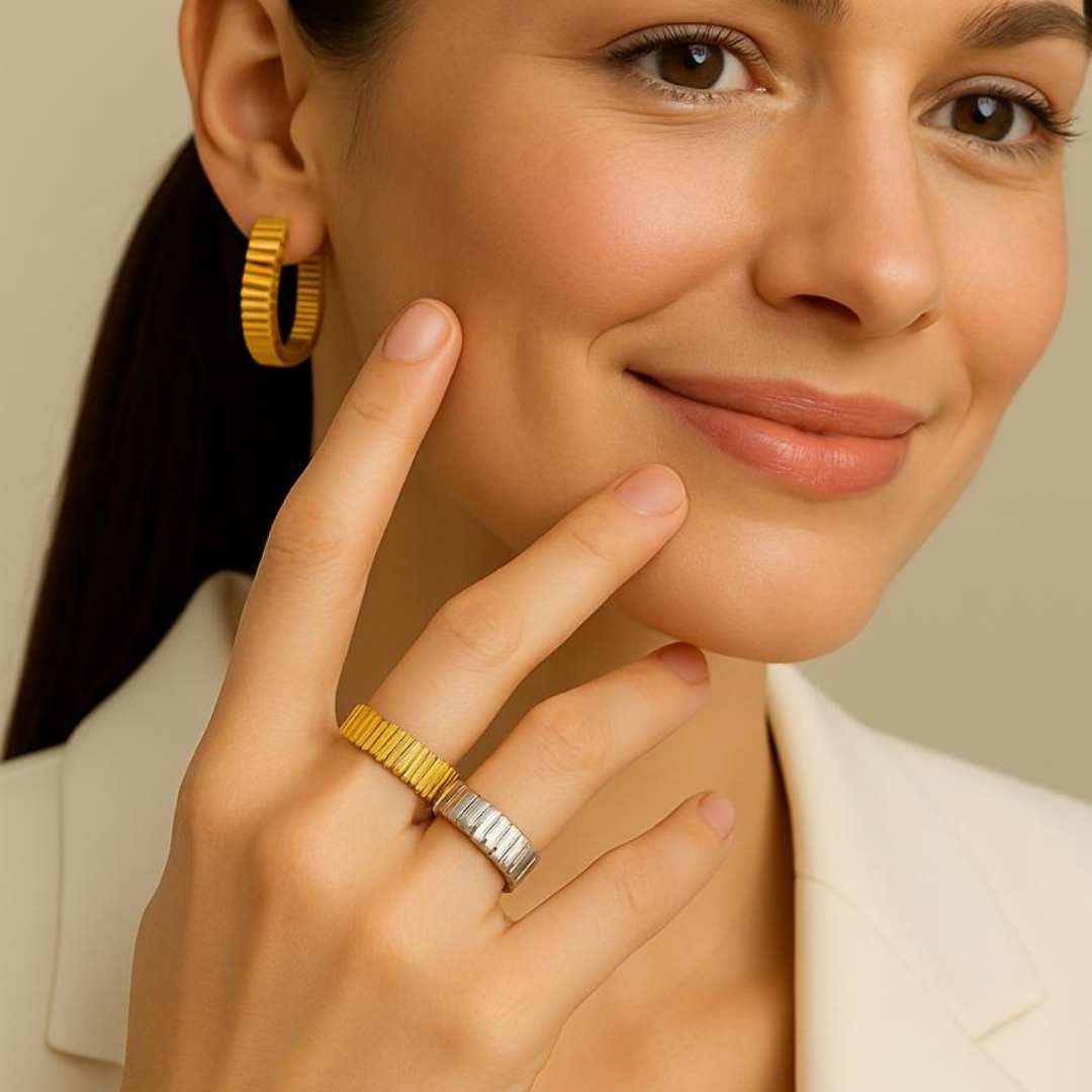 Woman wearing gold orbit hoop earrings and a gold ring, touching her face from House of Pehr