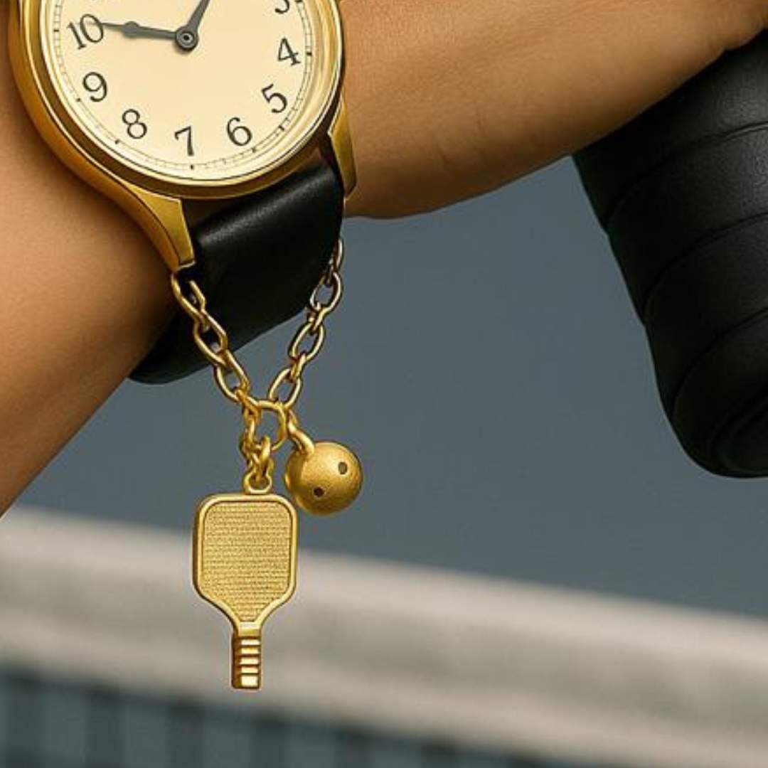 Gold watch charm with pickleball paddle and ball on a Watch against a blurred background
