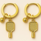 Gold hoop earrings with pickleball paddle and ball charms on a beige background