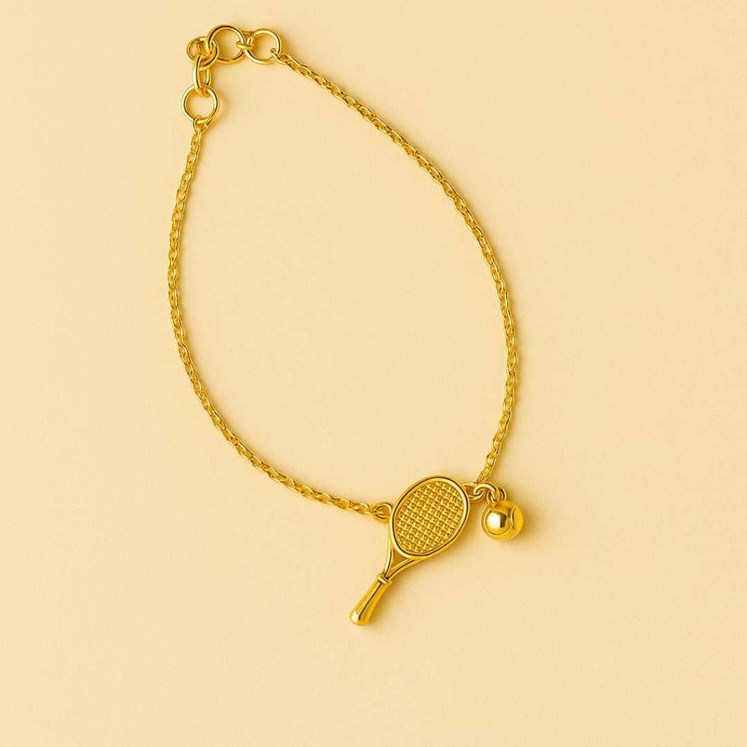 Gold bracelet with tennis racket and ball charm on a wrist against a beige background from House of Pehr