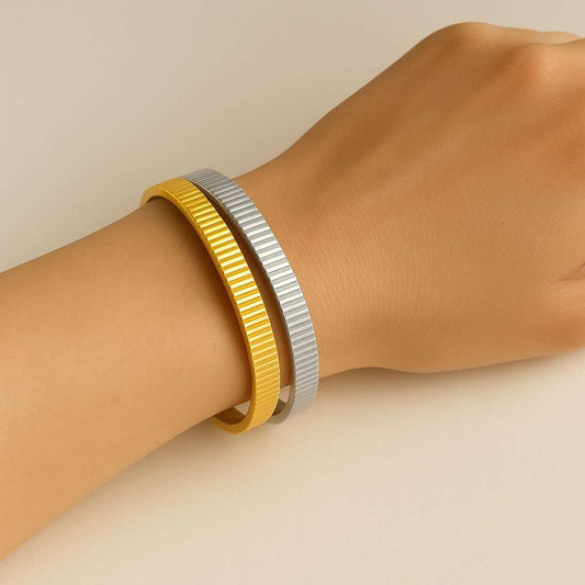 Hand wearing the orbit gold and silver bangle on a beige background from House of Pehr