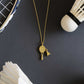 Gold necklace with a badminton racket pendant next to a badminton shuttlecock and racket on a dark surface from House of Pehr