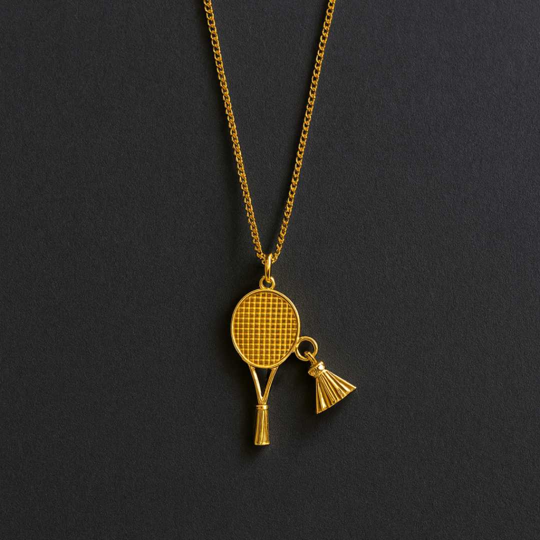 Gold necklace with a badminton racket pendant next to a badminton shuttlecock and racket on a dark surface from House of Pehr