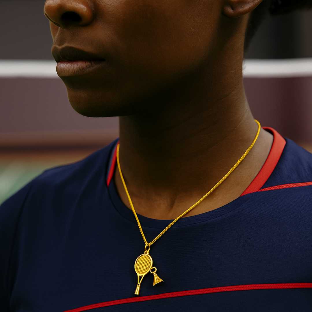 Gold necklace with a badminton racket pendant next to a badminton shuttlecock and racket on a dark surface from House of Pehr