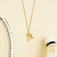 Gold necklace with a badminton racket pendant next to a badminton shuttlecock and racket on a dark surface from House of Pehr