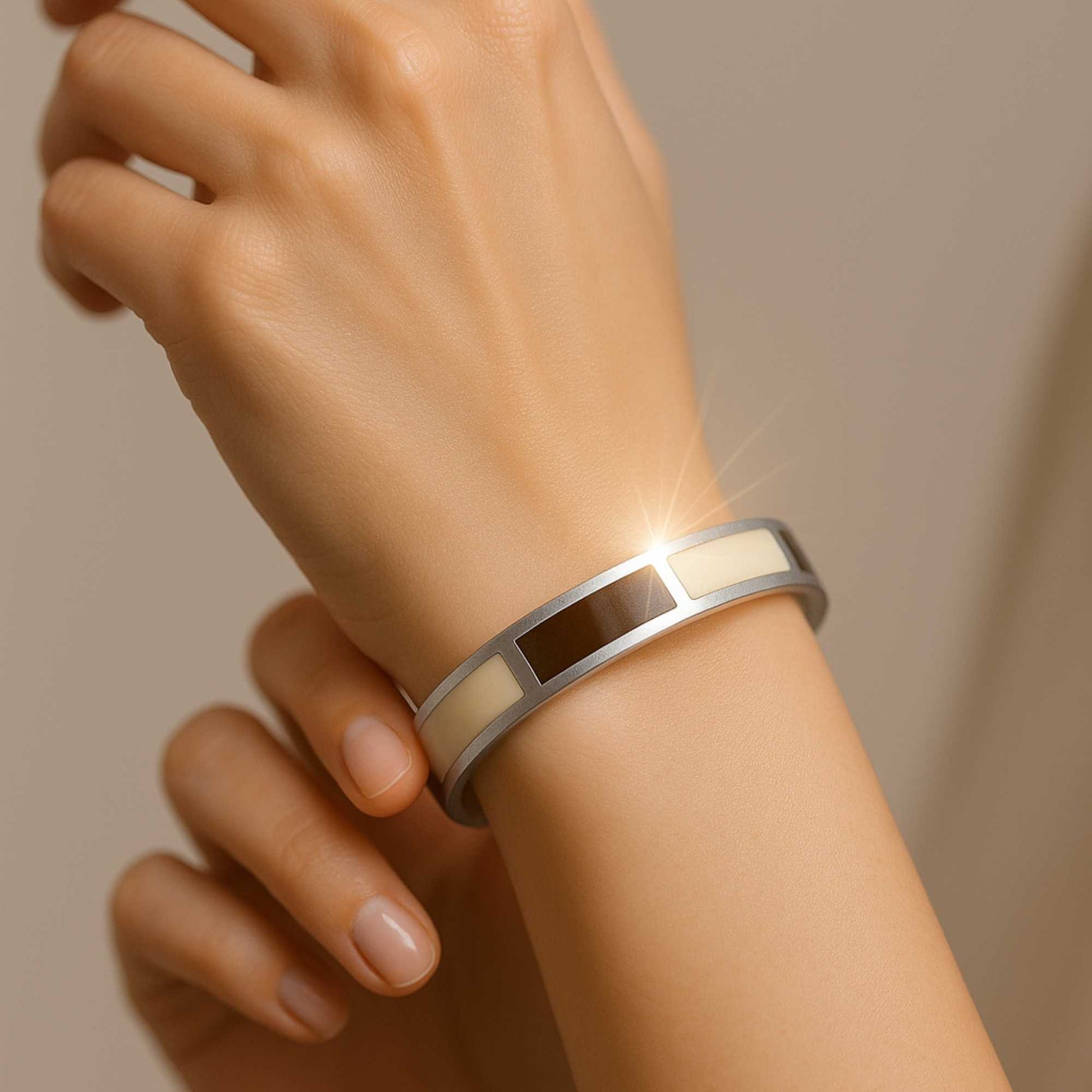 Close-up of a wrist wearing a silver bracelet with a dark brown center on a beige background. Dune bangle
