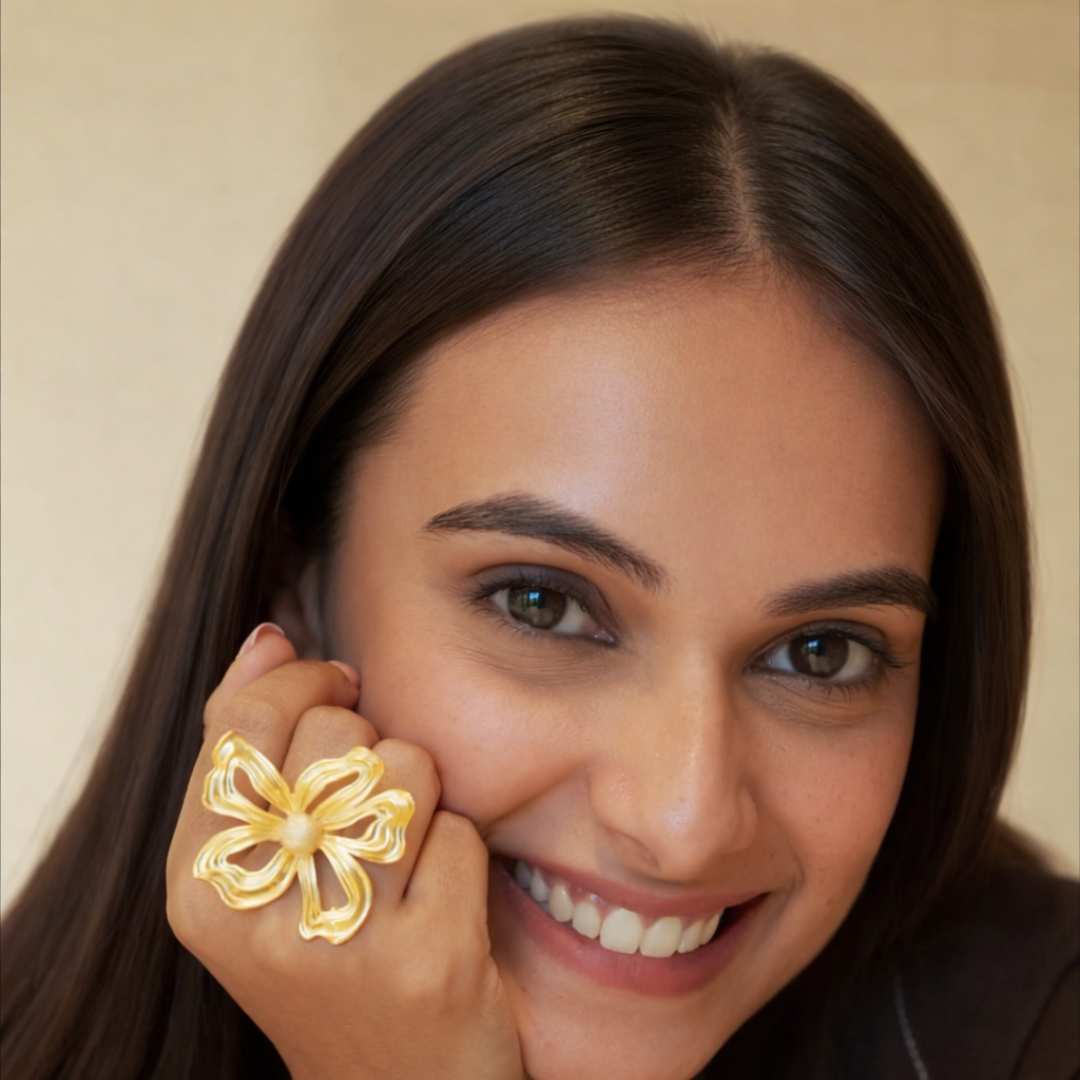 Woman wearing a gold floral earring with a beige background from House of Pehr 