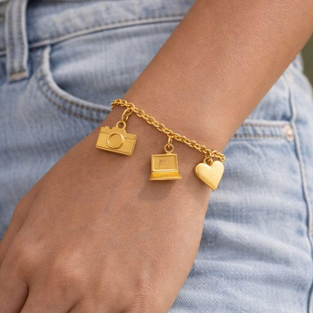 Gold bracelet with camera, laptop, and heart charms on a wrist against a denim background from House of Pehr  - Image 1