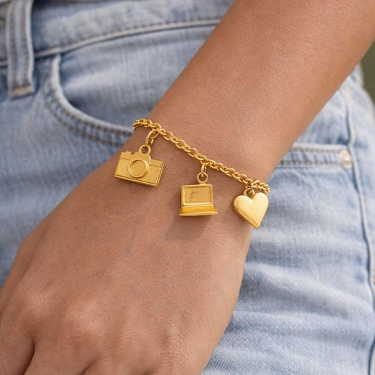 Gold bracelet with camera, laptop, and heart charms on a wrist against a denim background from House of Pehr 