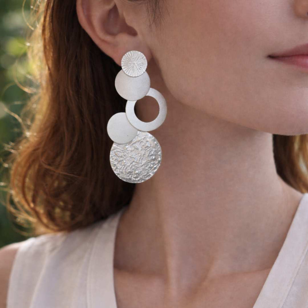 Close-up of a woman wearing silver circular earrings with a blurred background from House of Pehr - Image 3