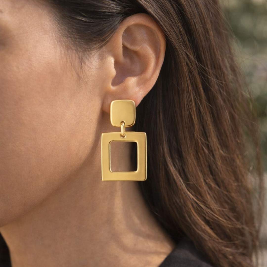 Gold square earrings worn by a person with blurred background from House of Pehr