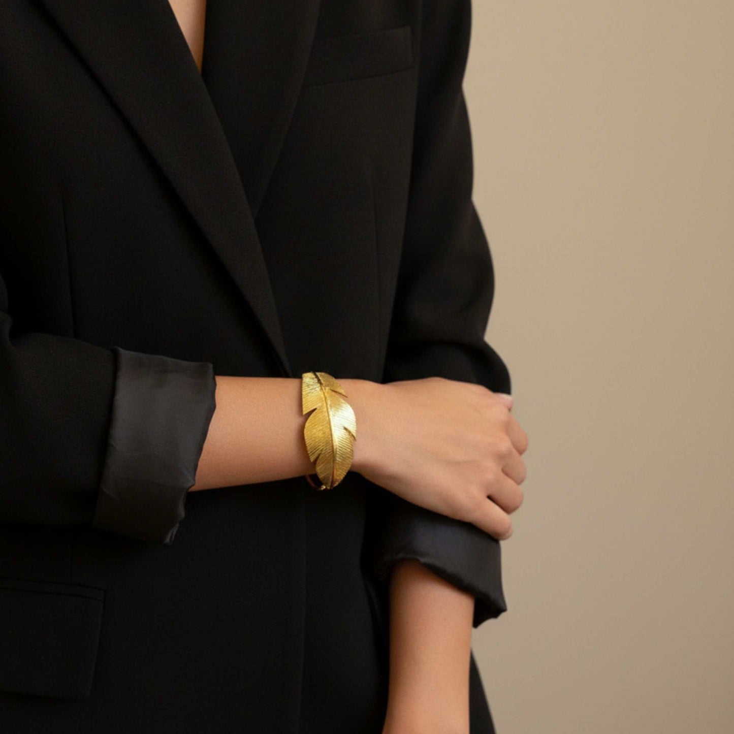 Person wearing a black blazer with a Gold feather-shaped cuff, Zephyr Cuff from House of Pehr