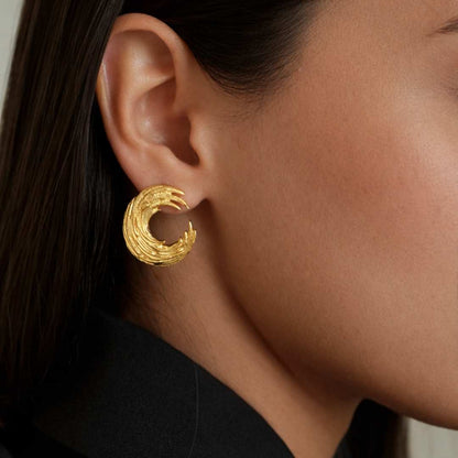 Close-up of a person wearing a gold earring with a textured design from House Of Pehr