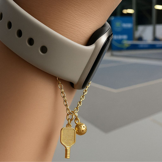 Gold watch charm with pickleball paddle and ball on a Watch against a blurred background