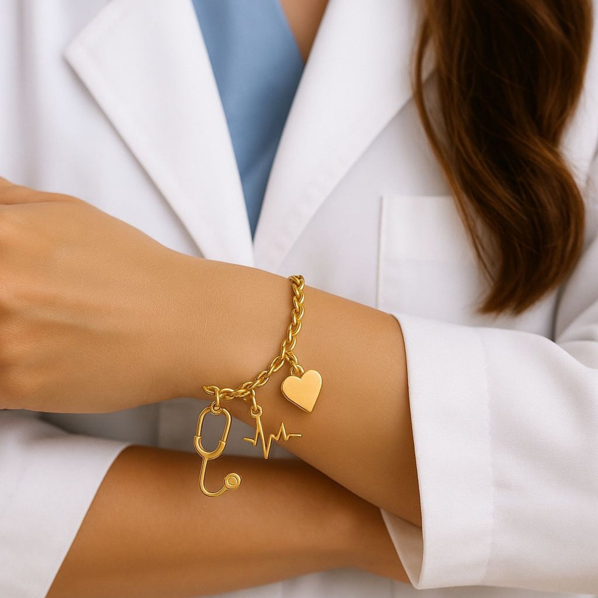Gold bracelet with medical-themed charms worn by a person in a white coat. Aceso bracelet from house of Pehr 