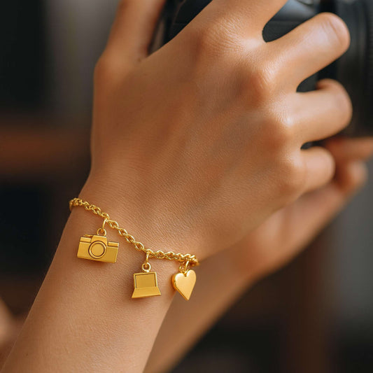 Gold bracelet with camera, laptop, and heart charms on a white background