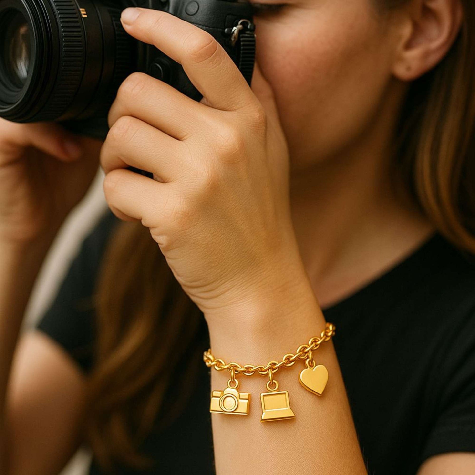 Gold bracelet with camera, laptop, and heart charms on a white background
