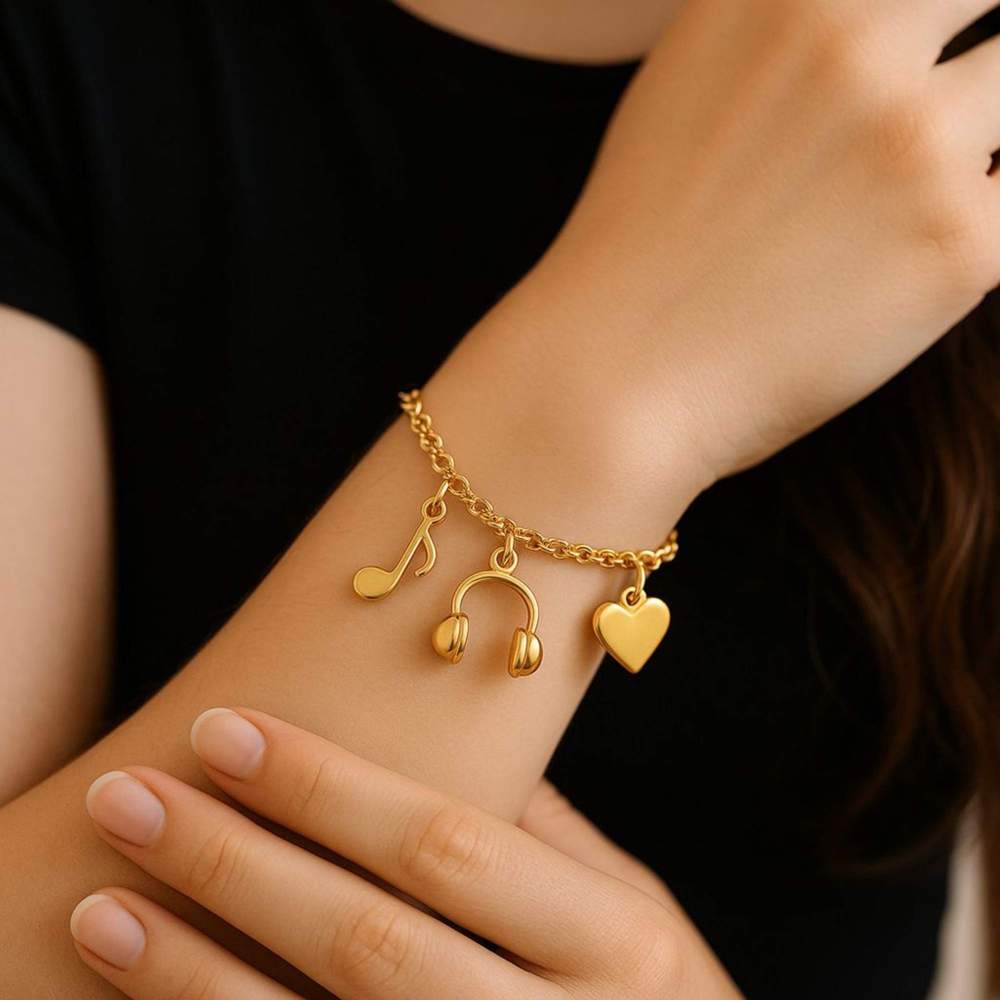Gold bracelet with music note, heart, and headphone charms on a wrist against a black background. Cadence Bracelet from House of Pehr