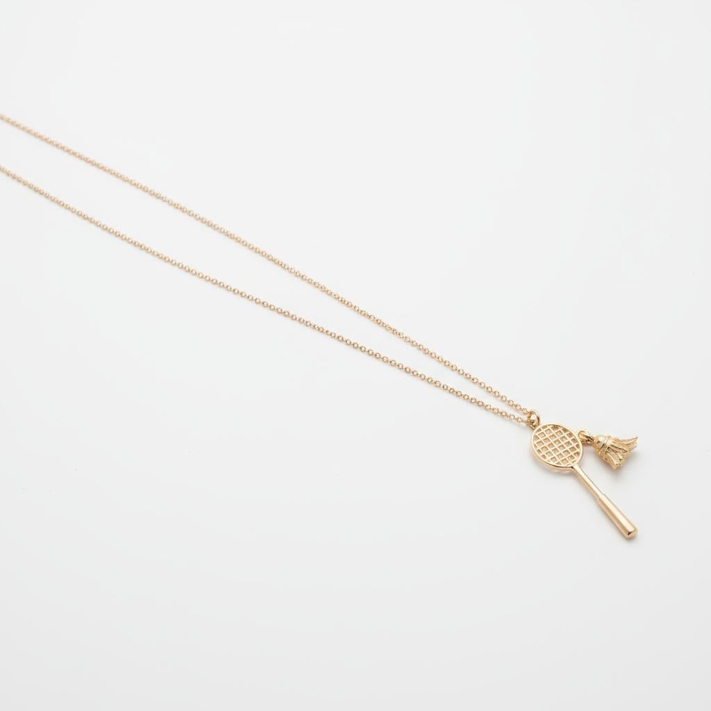 Gold necklace with a badminton racquet with shuttlecock pendant on a light gray background from House of Pehr