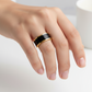 Hand wearing a black and gold ring on a light background