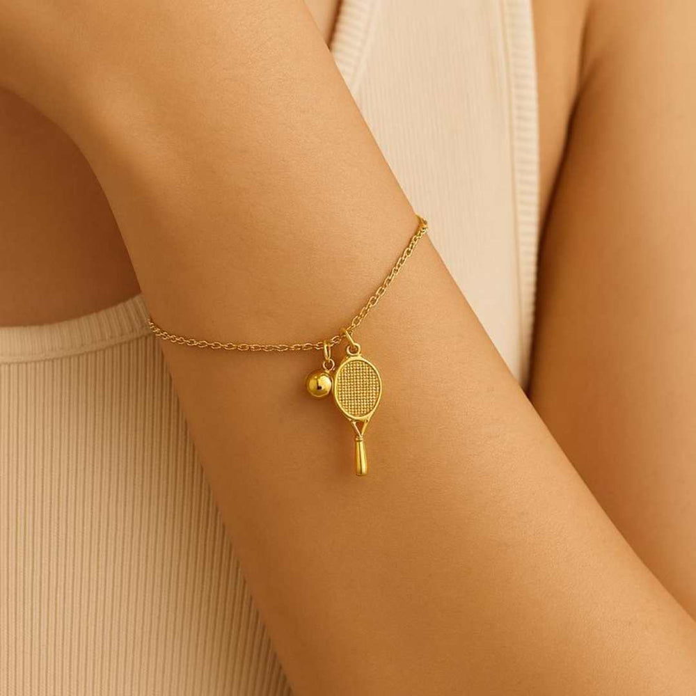 Gold bracelet with tennis racket and ball charm on a wrist against a beige background from House of Pehr - Image 5